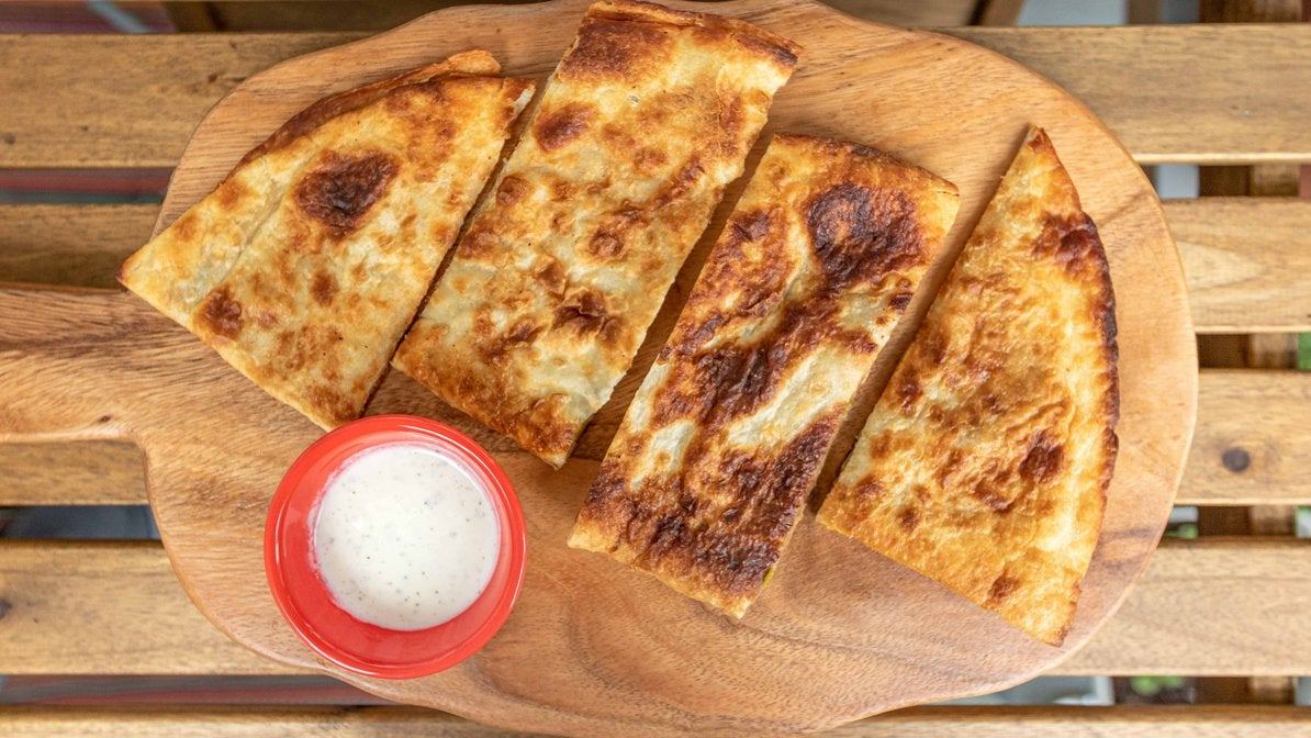 Bolani flatbread cut into wedges with yogurt dip