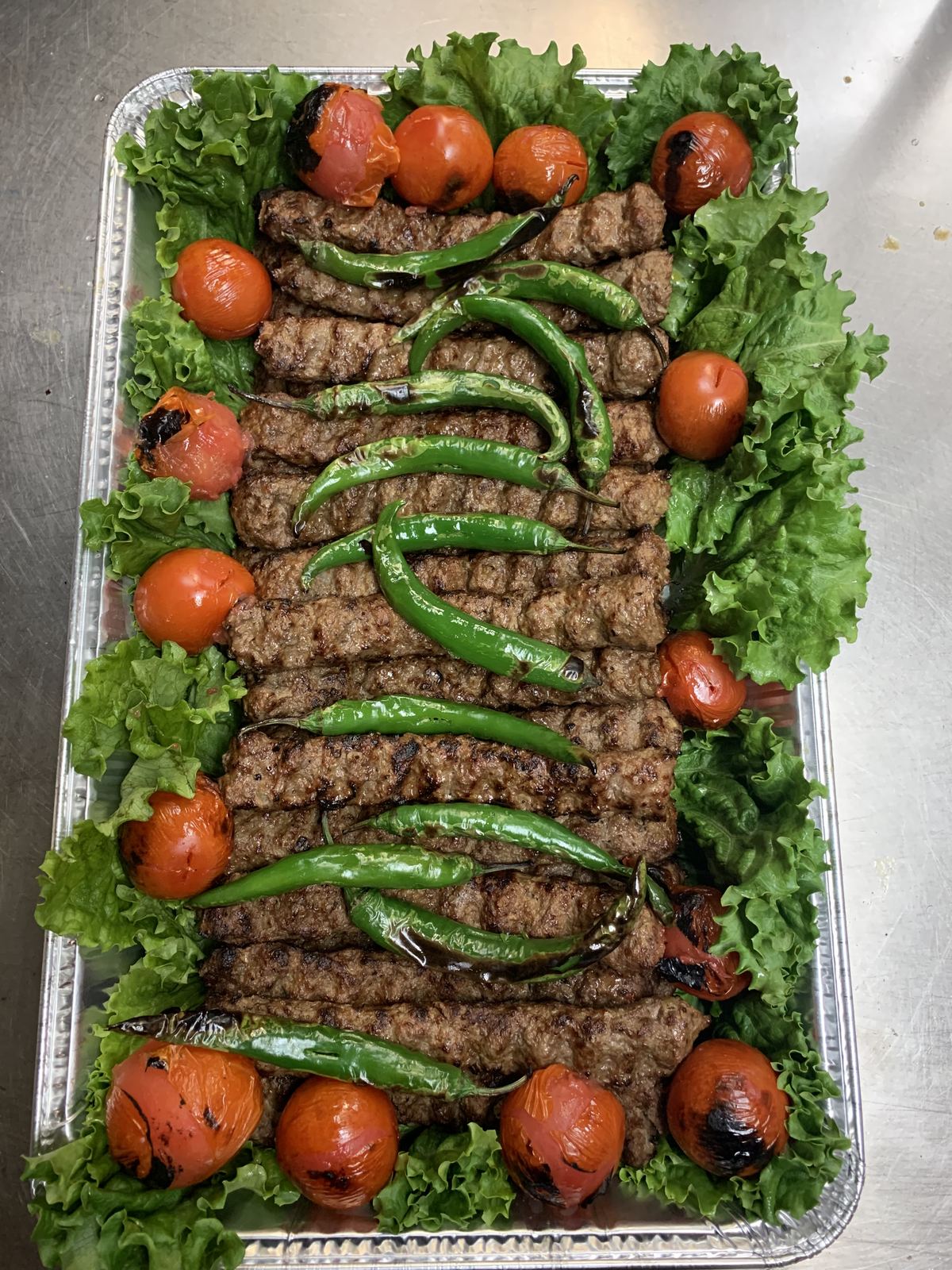 Catering tray of beef shami kabobs with grilled tomatoes and peppers